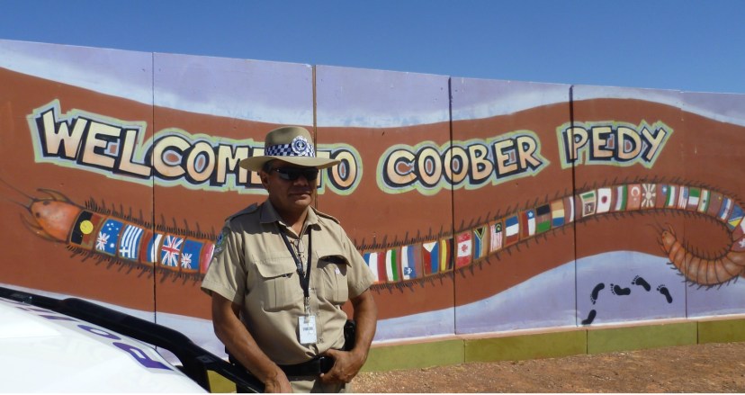 A police officer stands at the welcome sign in Coober Pedy